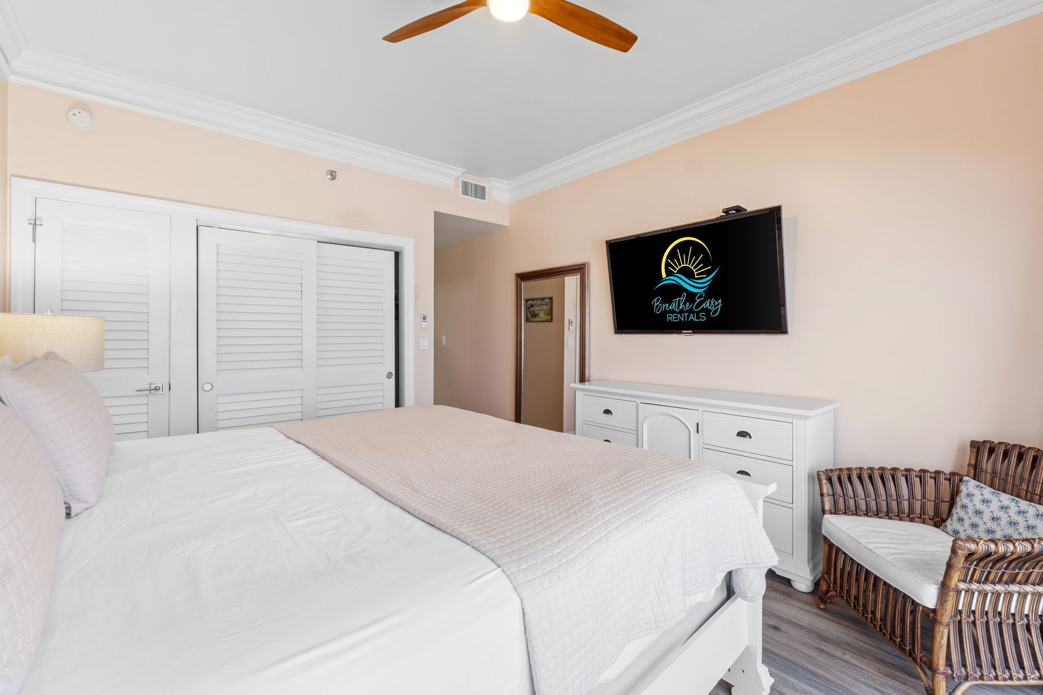 A bedroom with a large bed, a television, a wicker chair, and a white dresser.