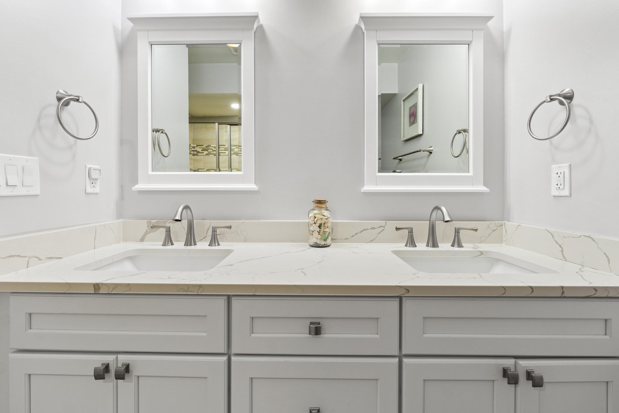 A bathroom with two sinks, a mirror above each sink, and a jar of toiletries on the countertop.