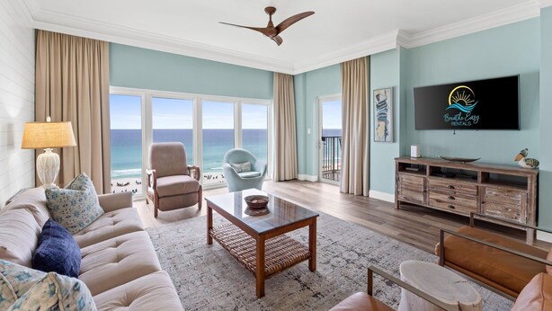 A living room with a view of the ocean, a ceiling fan, a television, and a wooden entertainment center.