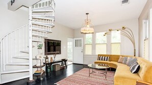 A spacious living room with a yellow sofa, a round coffee table, and a striped rug. A white spiral staircase leads to another room. - Spacious and Charming- Walk to Rainey Street (Austin)