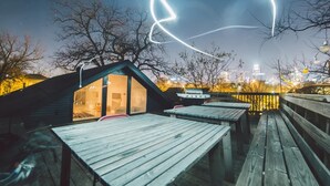 A rooftop bar with wooden tables and a grill, overlooking a cityscape at night. - Spacious and Charming- Walk to Rainey Street (Austin)