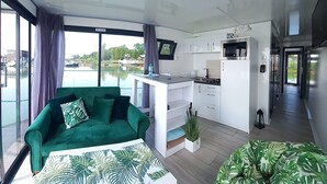 Una sala moderna con un sofá verde, una mesa de centro con estampado de hojas y vistas a un cuerpo de agua a través de amplias ventanas.