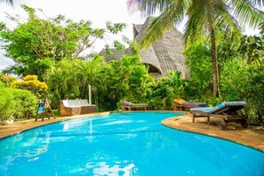 Une piscine entourée d’une végétation luxuriante et bordée d’une structure à toit de chaume.