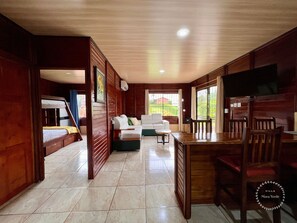 A spacious living area with a sofa, a dining table, and a TV. There is a staircase leading to a bunk bed area.