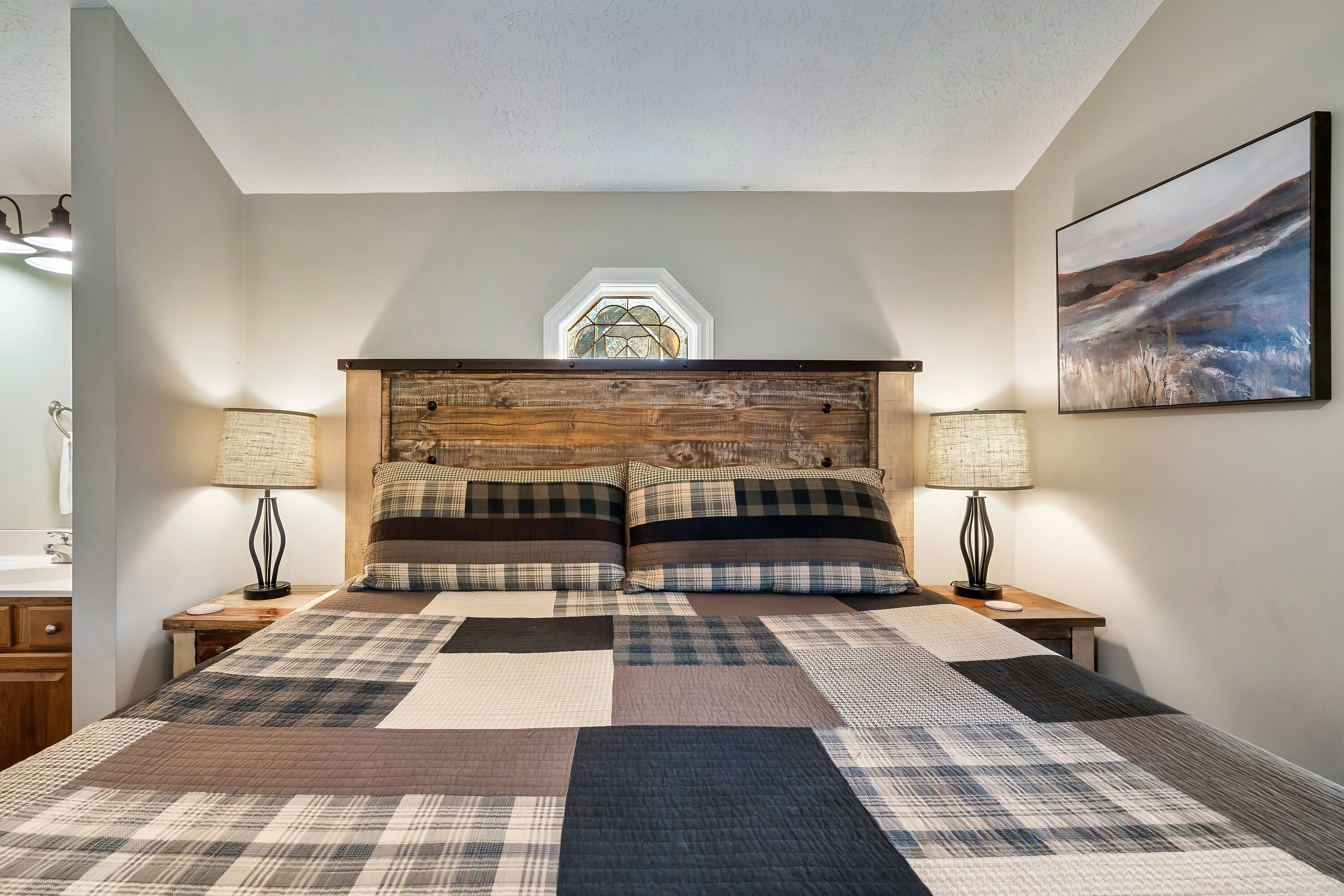 Un dormitorio con una cama grande, dos mesitas de noche, un cabecero de madera, una ventana y un cuadro en la pared.