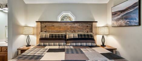 Un dormitorio con una cama grande, dos mesitas de noche, un cabecero de madera, una ventana y un cuadro en la pared.