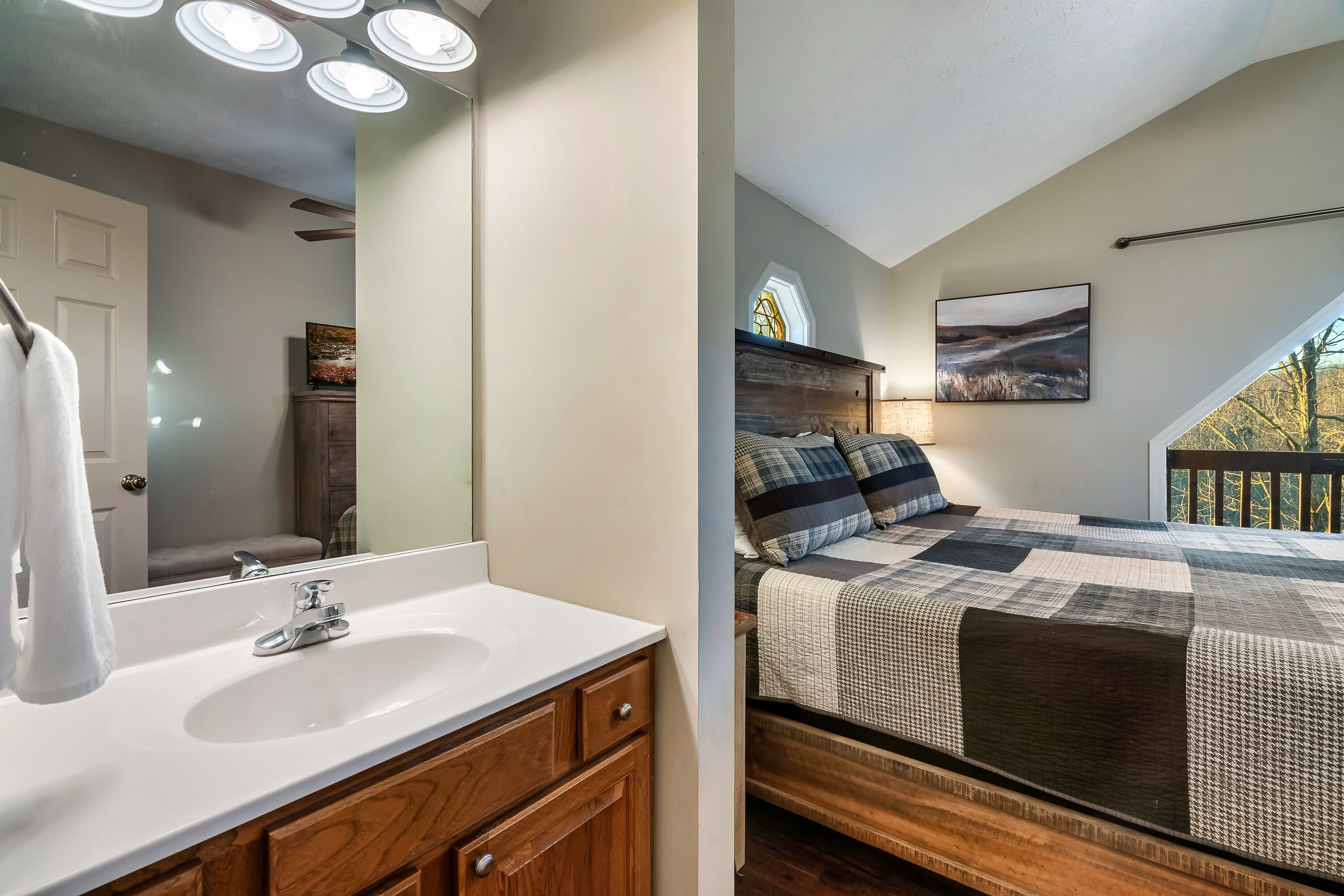 A bedroom with a large bed, a nightstand, a window with a view, and a painting on the wall.