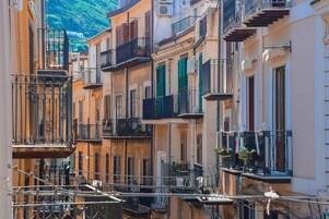 Una calle estrecha con edificios de varios pisos, balcones con barandillas y macetas con plantas.
