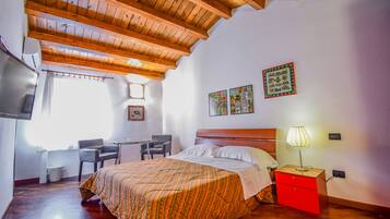 A bedroom with a wooden ceiling, a bed with a patterned bedspread, a nightstand with a lamp, and a desk with a chair.
