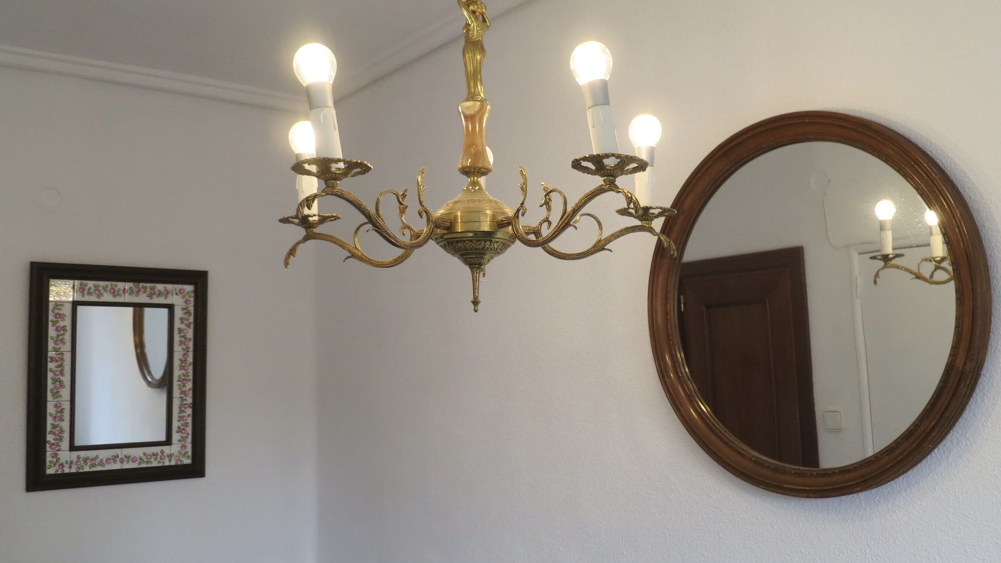 Un lampadario con quattro luci, un grande specchio e un quadro incorniciato appesi al muro.