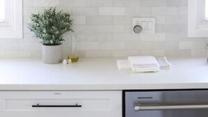 Una cocina con armarios blancos, estantes de madera y diversos utensilios de cocina.