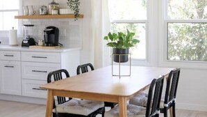 Una cocina moderna con armarios blancos, una mesa de comedor de madera, sillas negras, un sofá verde y una lámpara colgante de latón.