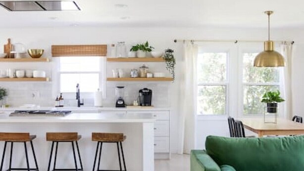 Una cocina moderna con una isla central, taburetes de bar y un sofá verde en un luminoso espacio de estar.