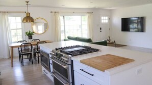 Una cocina moderna con una isla central, dos hornos, estufa a gas y un comedor con sillas y mesa.
