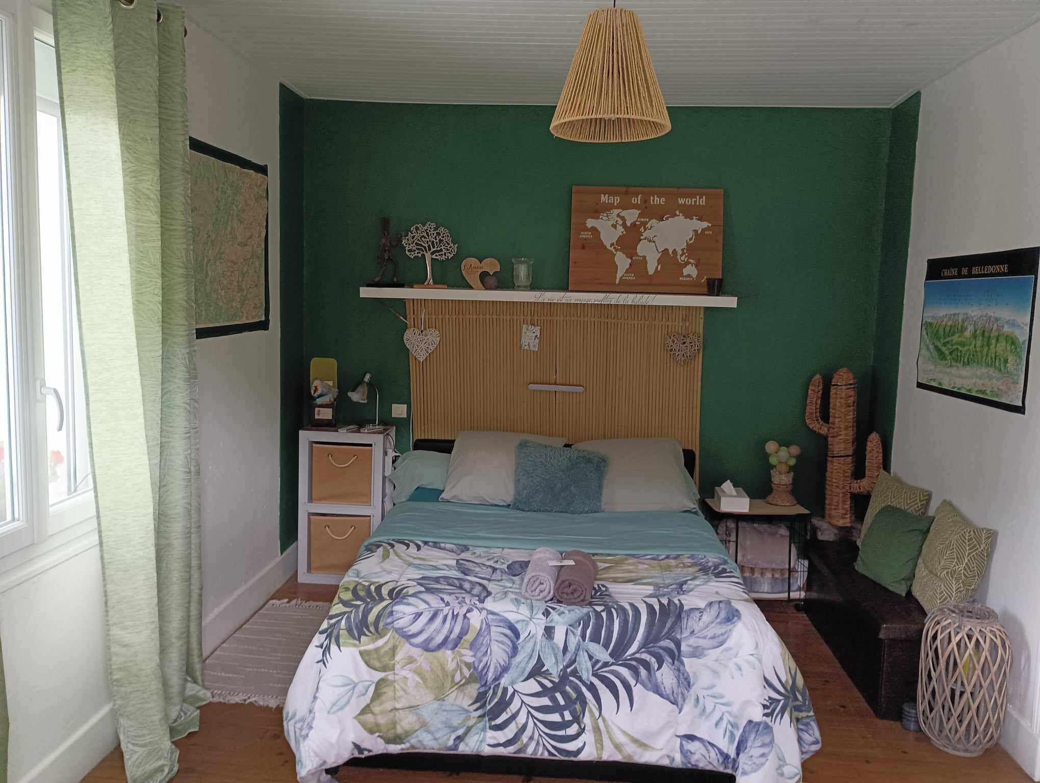 Quarto com cama, mapa-múndi, cacto e luminária pendente.