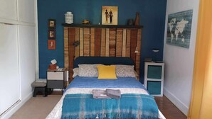 Una camera da letto con una testiera in legno, un letto con lenzuola blu, un comodino e una TV a parete.