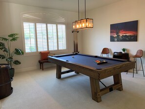 A pool table in a room with large windows, a ceiling light fixture, and a painting on the wall.