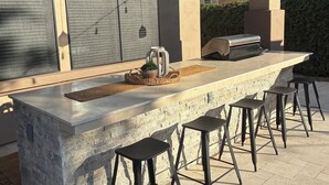 Eine moderne Außenküche mit einer Steineninsel, Barhocker und einem Grill.