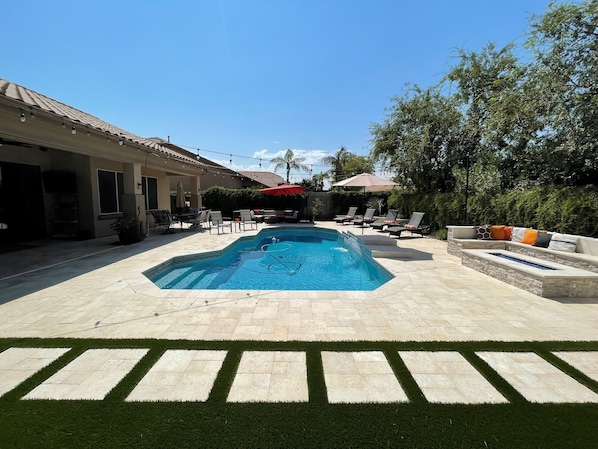 A swimming pool with a tiled deck, surrounded by lounge chairs and a covered seating area.