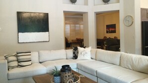 Ein Wohnzimmer mit einer Eckcouch, einem Couchtisch mit Dekorationselementen, einem großen abstrakten Gemälde und einer Wanduhr.