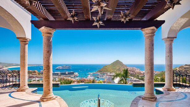 A pool area with clear blue water, surrounded by stone columns and a pergola with star-shaped decorations.
