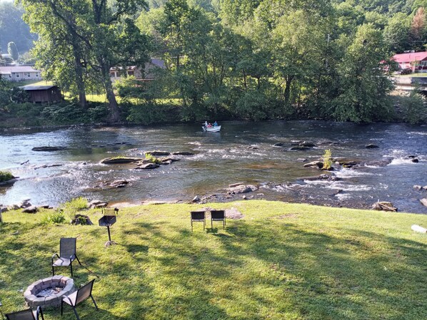 A river with a boat, surrounded by trees and a grassy area with chairs.