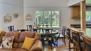 Amplia sala de estar con un sofá de cuero marrón, una mesa de comedor con sillas y una cocina con gabinetes de madera.