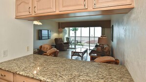 A kitchen with granite countertops, wooden cabinets, and a dining area with wicker furniture. - Beautiful Bonita Beach Front Condo, Casa de Mimi in Dolphin Way (Bonita Springs)