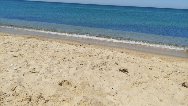 Une plage de sable fin, avec une eau d’un bleu limpide et un ciel dégagé.