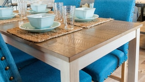 Un coin repas avec une table en bois, des chaises à l’assise rembourrée de tissu bleu et de la verrerie transparente.