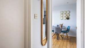 Una habitación con un espejo grande, una zona de comedor con mesa y sillas, y un adorno circular en la pared.