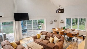 A spacious living area with a large sofa, a wooden coffee table, and a dining table set for six. - BearVaria AC, Hot Tub, Fire Pit Grill, FrisbeeGolf (Killington)