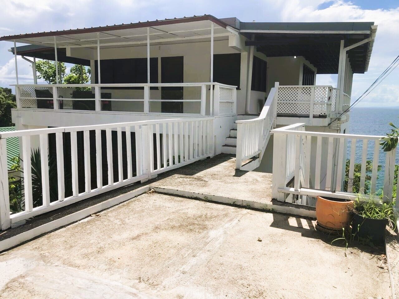 Un edificio de dos pisos con un balcón, barandillas blancas y vista al mar.