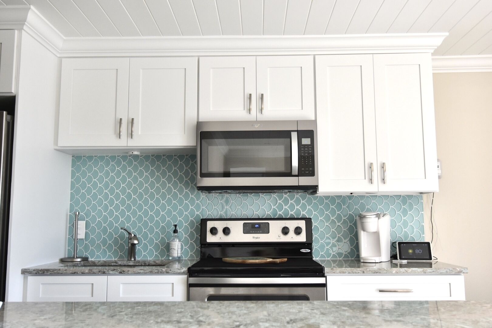 A kitchen with white cabinets, a microwave, a stove, and a coffee maker.