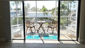 A balcony with a glass door, two wooden chairs, a small table, and a blue mat with a letter 'T' on it. - Beautiful Ocean Access Islamorada Condo. MM 76.5 Bring your Boat (Islamorada)