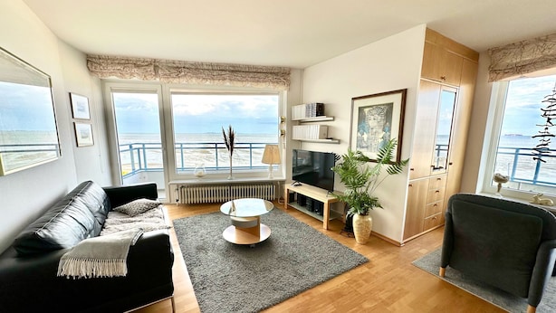 A modern living room with a black leather sofa, a glass coffee table, and a view of the sea through large windows. - Herring Gull - Fantastic sea view (Cuxhaven)