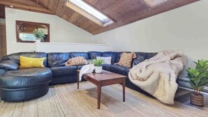 Un salon chaleureux avec un canapé d’angle, une petite table basse en bois et une grande fenêtre laissant entrer la lumière naturelle.