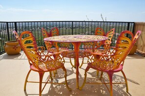 Een ronde buitentafel met stoelen, omringd door een zwart metalen hek, met uitzicht op een verafgelegen landschap.