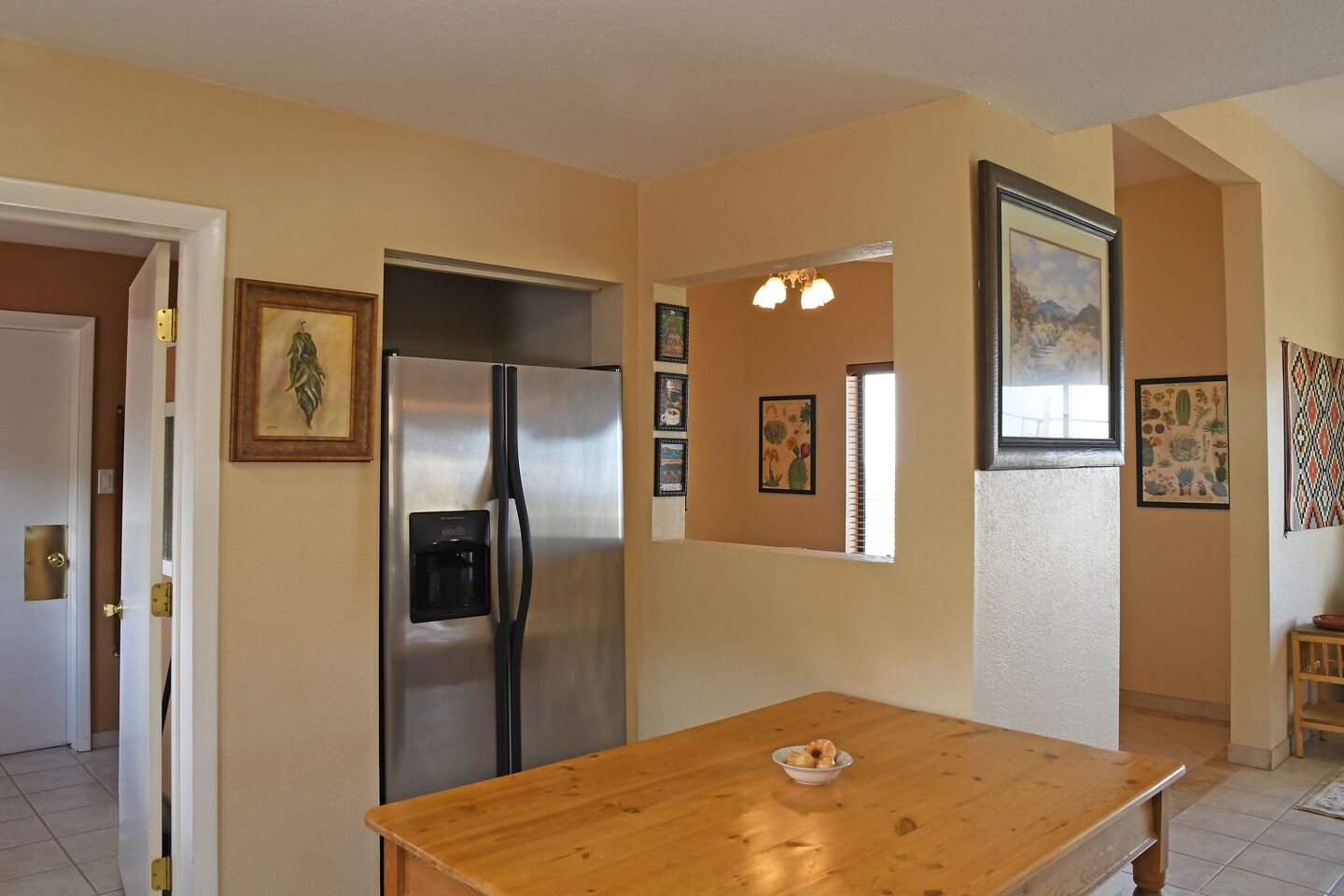 Una cocina con un refrigerador de acero inoxidable, una mesa de madera y varias fotografías enmarcadas en las paredes.