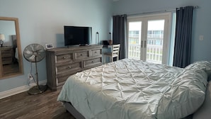 A bedroom with a bed, a dresser, a TV, a ceiling fan, and a window with curtains.