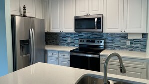 A modern kitchen with white cabinets, a stainless steel refrigerator, a microwave, an oven, and a sink with a faucet.