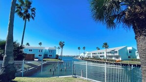 A waterfront property with a pool, palm trees, and a white fence.