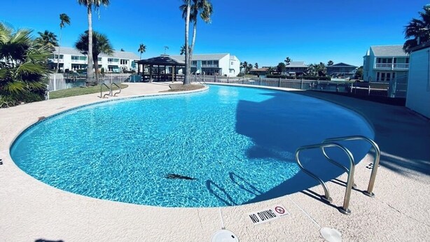 A swimming pool with a 'NO DIVING' sign, surrounded by palm trees and buildings.
