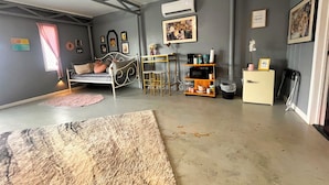 Une chambre à coucher de taille réduite, comprenant un lit, un petit bureau, une chaise et une étagère où sont rangés des objets personnels.