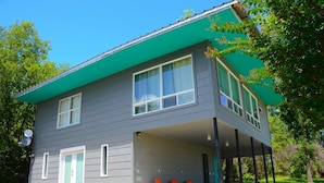 A two-story house with a green roof, a covered porch with orange chairs, and a satellite dish. - The Studio at Stardust Mid-Century Retreat (Coleman)