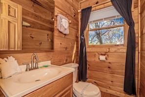 A wooden cabin bathroom with a sink, toilet, and window.