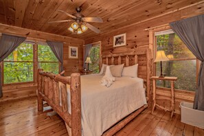 Camera da letto in una baita di legno, con un letto, una ventola a soffitto e ampie finestre.