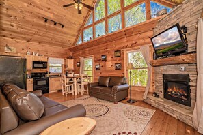 A cozy cabin interior with a fireplace, wooden walls, a sofa, and a television.