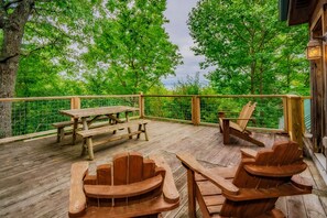 Un pontile in legno con tavolo da picnic e poltrone Adirondack, circondato da una ringhiera in legno e alberi.