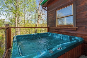 A hot tub on a wooden deck with a window overlooking a forest.